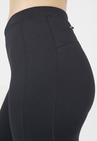 Svarta högmidjade leggings i elastisk tyg, med platta sömmar och en liten ficka på sidan för förvaring.