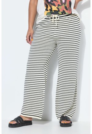 Persona che indossa pantaloni in maglia a righe bianche e nere a gamba larga con vita regolabile e sandali neri scivolati.