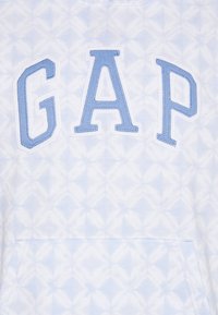 Felpa azzurra chiara con la parola "GAP" in evidenza, ricamata in lettere più grandi. Sfondo con un motivo geometrico bianco e una tasca frontale.