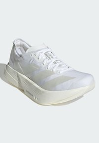 Basket blanc de sport avec dessus en maille, lacets plats et trois rayures diagonales. Il présente une semelle épaisse et rembourrée pour un soutien et un confort optimal.