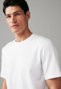 Witte katoenen t-shirt met een ronde hals en korte mouwen, gladde textuur, taillering en subtiele stikseldetails.