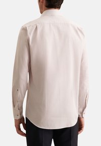 Camicia a maniche lunghe in tessuto rosa chiaro con piccoli pois scuri, dotata di colletto classico e polsini con bottoni, con orlo curvo.