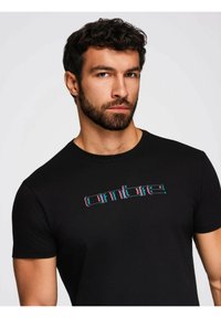 Sort kortærmet t-shirt med rund halsudskæring og flerfarvet broderet tekst "ombre" på brystet. Blødt, tætsiddende stof.
