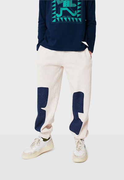 Jogginghosen aus Baumwollmix in hellem Creme mit dunkelblauen Akzentflecken. Sie verfügen über einen lockeren Schnitt, einen elastischen Bund und Seitentaschen.