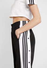 Svartvita träningsbyxor med knäppknappar på sidorna, resårmidja och svarta ränder längs sidorna.