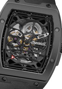 Zwarte, rechthoekige horloge met een open ontwerp, metaalachtige tandwielen zichtbaar van binnen en een rond logo. Heeft witte en rode wijzers en een gestructureerde band.