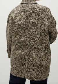Giacca oversize in stampa leopardata con colletto, caratterizzata da una combinazione di colori beige e nero, texture morbida e polsini abbottonati.