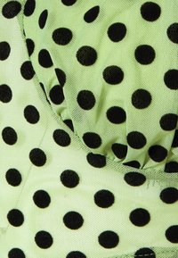 Mintgrüner Stoff mit großen schwarzen Punkten. Das Material ist weich und strukturiert und weist eine geraffte Detailgestaltung auf.