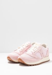Une paire de baskets en daim et en mesh rose clair avec des lacets blancs et des semelles crème, positionnées côte à côte sur une surface blanche.
