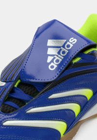 Chaussure de sport Adidas bleue avec des accents vert néon, des lacets noirs et une bande à scratch avec le logo Adidas.
