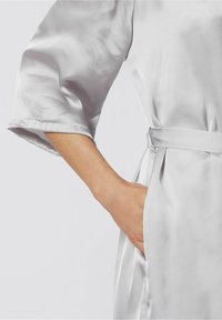 Rochie din satin gri deschis cu mâneci late, având un brâu și buzunare. Textură netedă cu un luciu subtil.