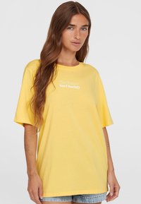Gele oversized t-shirt gemaakt van katoen met korte mouwen, voorzien van witte tekst "The Future Surf Society" op de borst.