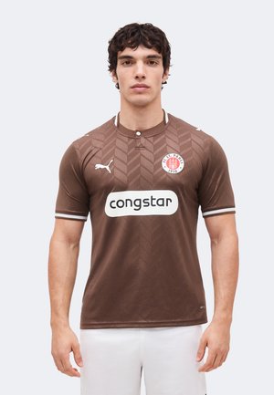Homme portant un maillot de football marron avec des bordures blanches, logo Puma, sponsor « congstar » et emblème du club FC St. Pauli 1910.