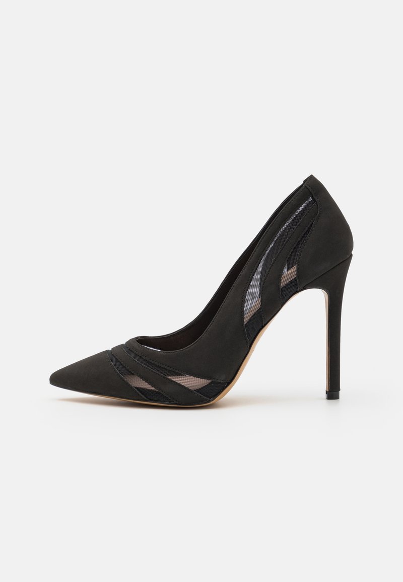 Escarpin noir à talon haut et bout pointu avec des détails en mesh sur les côtés et à l'avant, présenté sur un fond clair uni.