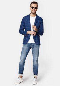 Niebieska, w kratkę marynarka na białej koszulce, w połączeniu z jasnoniebieskimi, przetartymi dżinsami i białymi trampkami. Model w okularach przeciwsłonecznych.