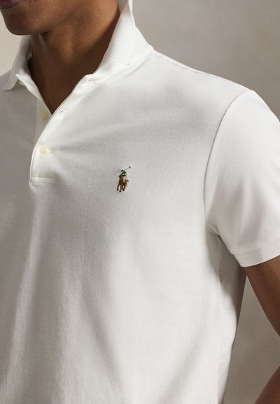 Férfi fehér galléros pólóingben, bal mellrészen kis hímzett polo játékos lóháton logóval.