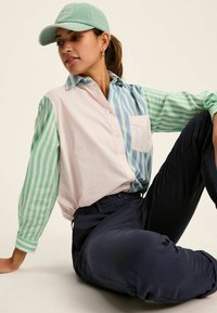 Koszula z wielokolorowym wzorem, w green i blue paski z różowym boku, połączona z granatowymi spodniami i jasnooliwkową czapką.