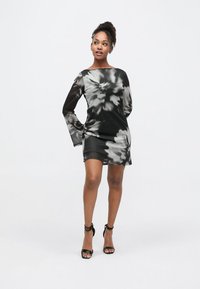 Vestido tie-dye preto e cinza com mangas compridas, decote barco e silhueta ajustada, combinado com sandálias pretas de salto alto com tiras.