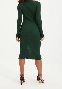 Robe longue ajustée à côtes de couleur vert foncé avec un col montant et des manches longues, associée à des sandales à talons hauts en imprimé léopard.
