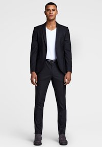 Black suit with a single button, paired with a white V-neck t-shirt. Slim-fit trousers and grey ankle boots complete the look.