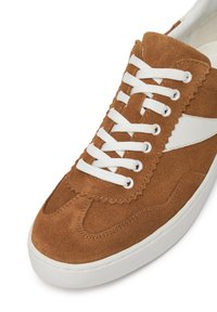 Tenis cu piele întoarsă maro, cu design alb de șireturi, margini ondulate și o dungi albă pe lateral. Prezintă un vârf rotund și o suprafață texturată.