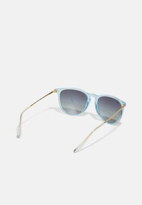 Ochelari de soare bleu deschis cu ramă transparentă, lentile gri cu degradé și accente metalice aurii pe temples și vârfuri.