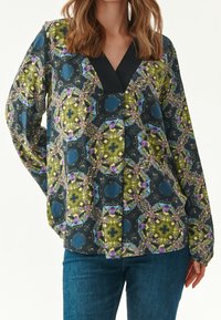 Blusa multicolore con motivo floreale e geometrico, maniche lunghe e scollatura a V con accento nero. Realizzata in tessuto leggero.
