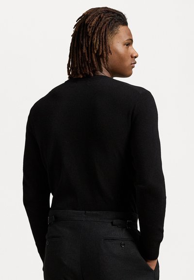 Pull en tricot noir à manches longues avec un col rond, vu de dos, associé à un pantalon noir ajusté avec une ceinture et des poches.