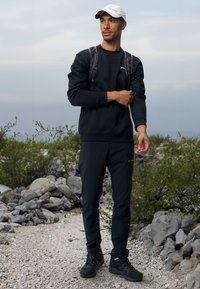 Sweat-shirt noir et pantalon, en matière synthétique, au design ajusté. Bottes de randonnée noires, avec des sangles de sac à dos réglables, casquette blanche avec logo.