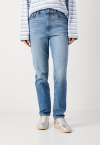 Lichtblauwe denim jeans, rechte pijpdesign, vijf-pocketstijl, middelmatige wassing met vervaagde gebieden, gedragen met zilveren sneakers.