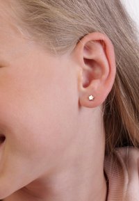 Gouden stervormige oorbel op een neutrale huidtoon, met een glanzende afwerking. De oorbel is klein en discreet, waardoor de natuurlijke vorm van het oor wordt benadrukt.