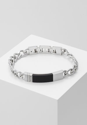 Silver chain bracelet with rectangular black textured plate engraved with "FOSSIL" on a white display surface.