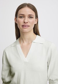 Pullover verde chiaro con scollatura a V e colletto a punta. Presenta maniche a sbuffo e materiale lavorato a maglia testurizzato. Design semplice e raffinato.