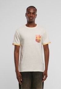 Camiseta de color crema con un acabado texturizado, que presenta un bolsillo con un patrón colorido y acentos vibrantes en las mangas.