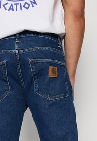 Mørkeblå denimjeans med en brun lærlogo-lapp på baklommen og kontraststing, som viser en tettsittende silhuett.