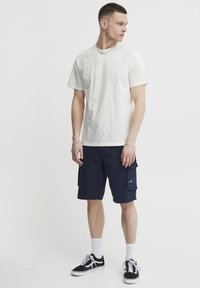 Lys beige t-skjorte med korte ermer kombinert med marineblå cargo-shorts, med sidelommer, og brukt med hvite sokker og svarte joggesko.