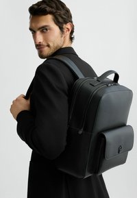 Zaino in pelle nera con finitura testurizzata, doppi zip, manico superiore e una tasca frontale con chiusura a scatto.