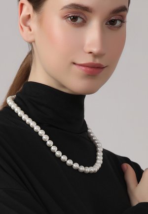 Weiße Perlenkette mit glatten, runden Perlen in unterschiedlichen Größen, über einem schwarzen Rollkragenoberteil getragen. Die Textur ist glänzend und einheitlich.