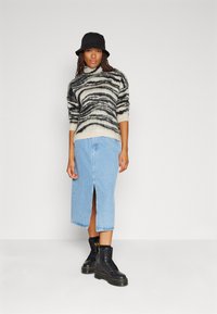 Gestreifter, schwarz-weißer, flauschiger Pullover, hellblaue Jeans-Bleistiftrock mit Schlitz vorne und schwarze schnürbare, klobige Stiefel. Schwarzer Bucket Hat.