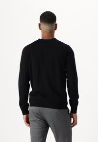 Černý pletený svetr s kulatým výstřihem a dlouhými rukávy, v kombinaci s šedými strukturovanými kalhotami. Střih je volný s žebrovanými manžetami.