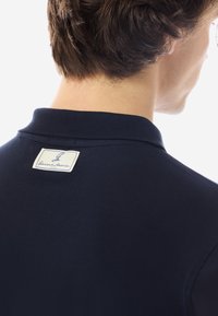 Dunkelblaues Poloshirt aus strukturiertem Baumwollstoff, mit einem gestickten Etikett am Kragen und einem klassischen Kragen-Design.