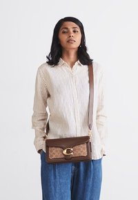 Brown crossbody bag with a textured tan panel featuring a signature pattern, gold hardware, and an adjustable strap.