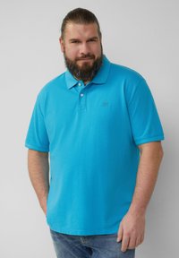 Polo bleu clair en tissu texturé, à manches courtes et avec une patte de boutonnage à trois boutons. Présente un emblème sur la poitrine gauche.