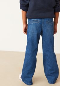 Blauwe denim jeans met een losse pasvorm, twee achterzakken en een rechtlopende snit, gecombineerd met witte sneakers. Eenvoudige stikdetails.