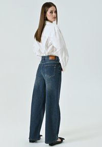 Lichte denim jeans met wijde pijpen en een hoge taille. Licht vervaging en twee achterzakken. Gedragen met een oversized witte blouse en zwarte ballerina's.
