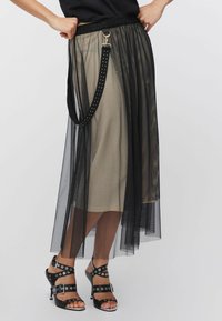 Gonna in rete nera con sottofondo beige, dotata di una fascia larga in vita e una cintura borchiata applicata. Sandali neri con tacco a blocco completano il look.