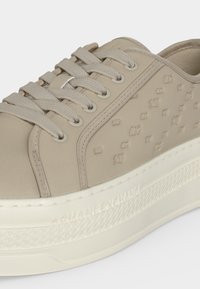 Baskets beige avec motif texturé et logo embossé sur une semelle blanche épaisse, avec lacets beige et détails cousus.