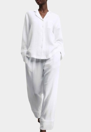 Weißes, strukturiertes Schlafset aus Baumwolle mit Hemd zum Knöpfen und Tasche sowie locker sitzender Hose mit breiten Bündchen.
