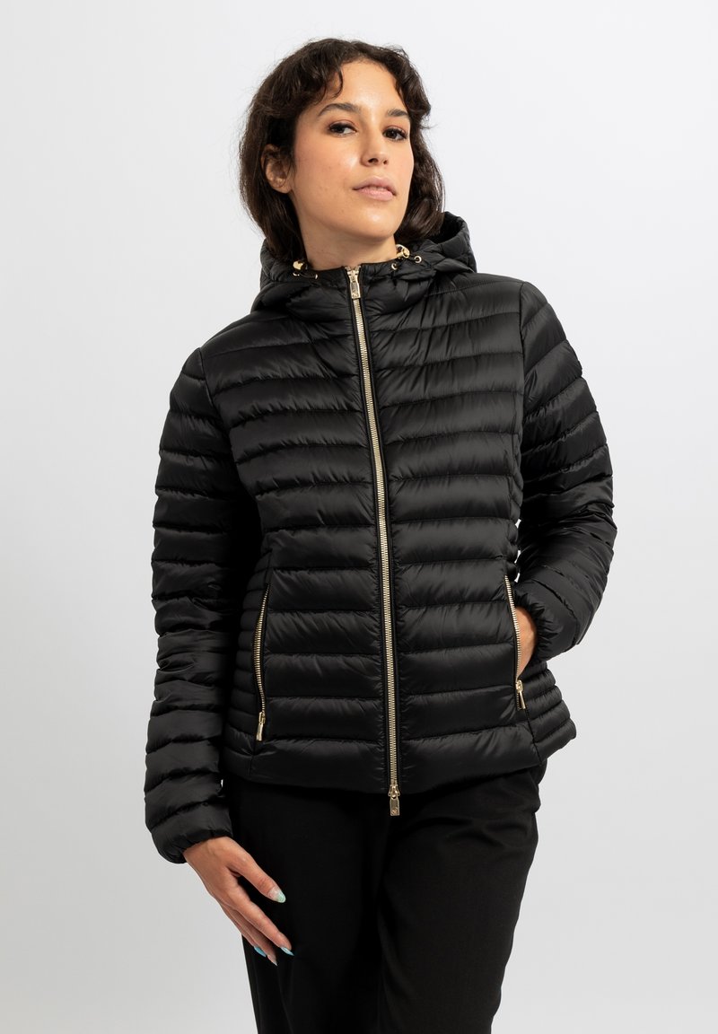 Giacca a piumino nera con cappuccio, caratterizzata da una texture trapuntata, dettagli con cerniera dorata e tasche laterali. Materiale liscio e leggero.