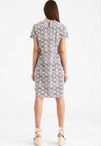 Polvassa pituinen mekko geometrisella painatuksella tummansinisenä ja vaniljana. Lyhyet hihat, pyöreä pääntie ja avainaukko yksityiskohtana selässä.